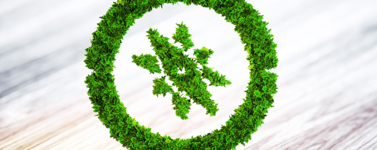 Um símbolo verde, feito com folhas e vegetação, representa um círculo com uma árvore estilizada no centro. Esse elemento visual remete à neutralidade de carbono, destacando práticas sustentáveis e o compromisso com a compensação de emissões de CO₂. A imagem sugere harmonia entre progresso e meio ambiente, simbolizando ações como reflorestamento, uso de fontes renováveis e a busca por um equilíbrio ecológico em prol da preservação do planeta.